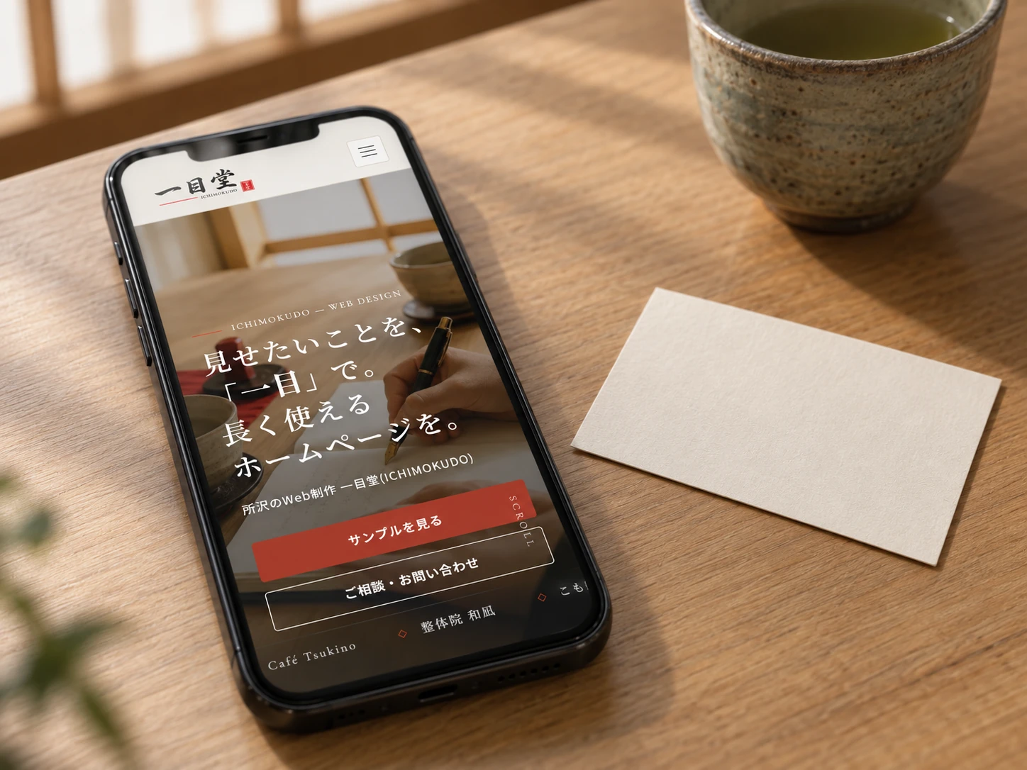 机に置かれたスマートフォンにホームページが表示され、横に名刺が一枚置かれている